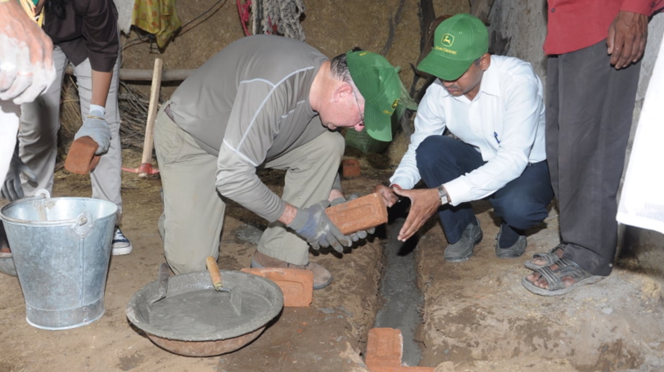 John Deere CEO Sam Allen assists farmers by laying bricks to build a trough in rural India.