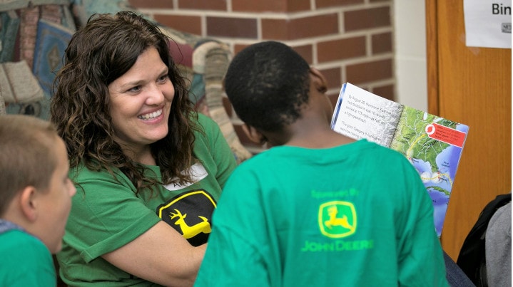John Deere employee smiles as she reads book to children.
