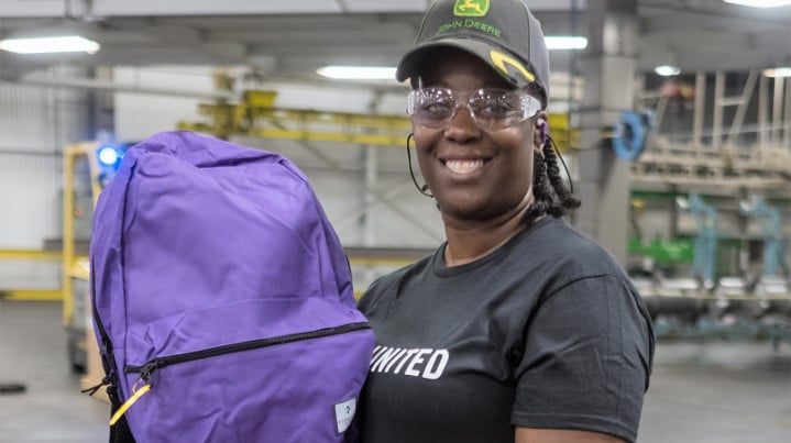 Smiling woman in factory holding a backpack.