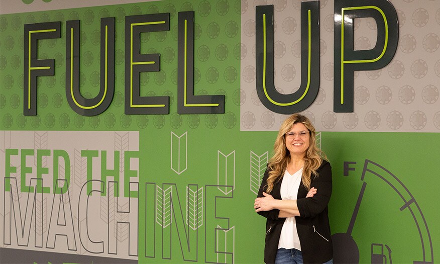 Portrait of Peggy Bliss in front of a sign that says "Fuel Up, Feed the Machine"