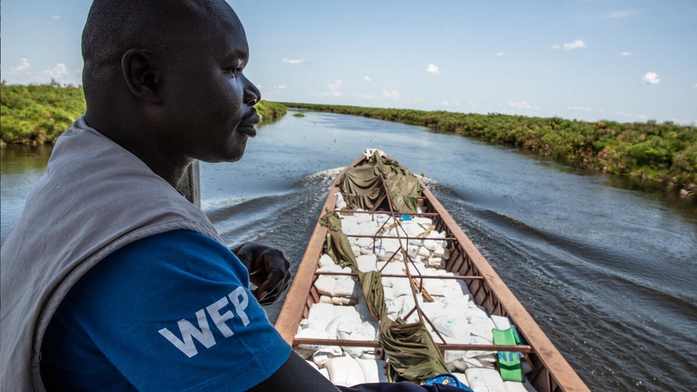 A man wearing a World Food Program shirt manages a boat with supplies onboard