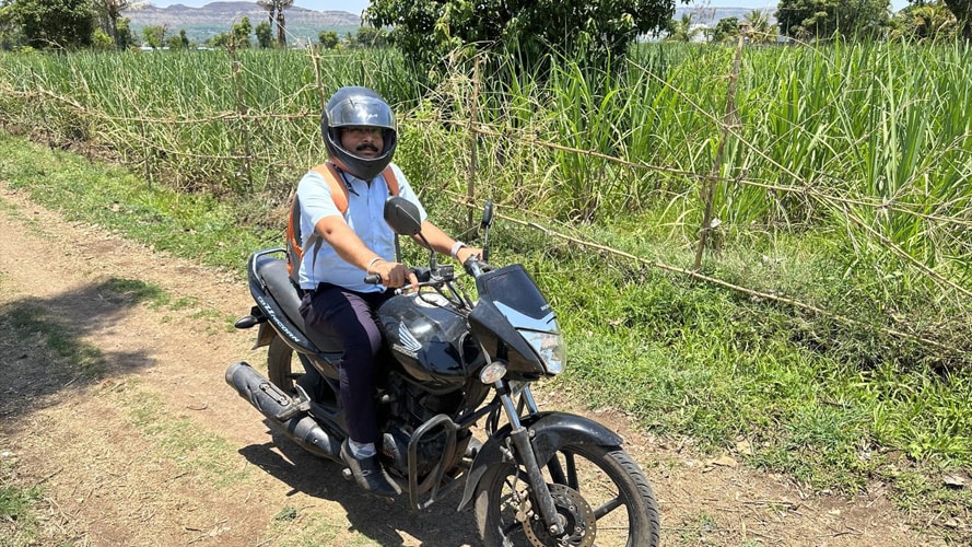 Man sits atop a motorcycle by a farm in India