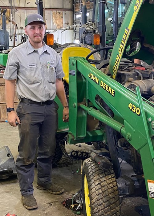 A Gator Wars participant stands next to a John Deere machine.