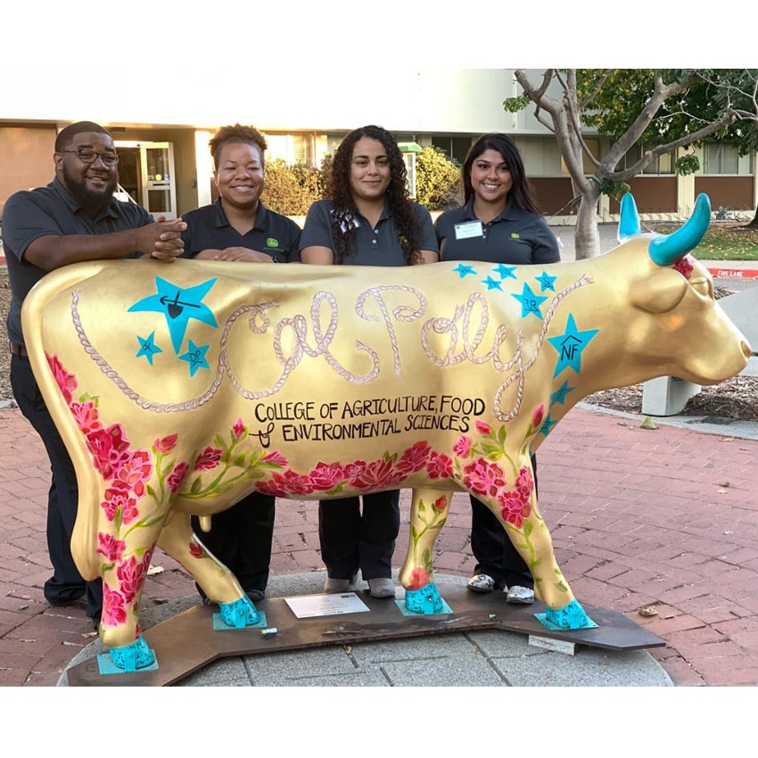 Jericho poses with colleagues behind a statue of a cow with text promoting "Cal Poly" college of food and environmental sciences