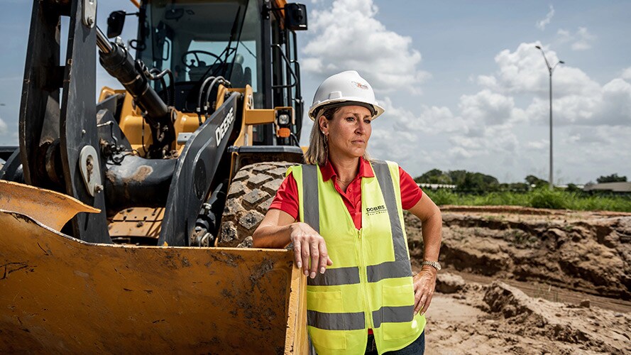 A construction employee stands proudly by their John Deere construction equipment