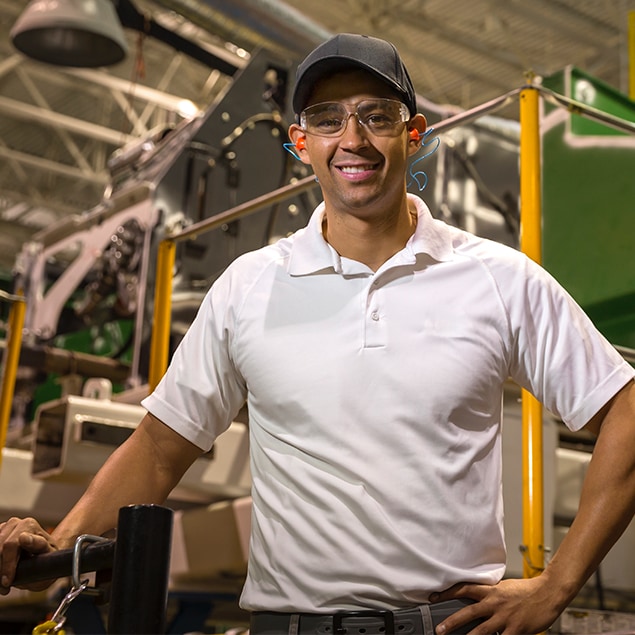 Hispanic man wearing protective eye wear and ear protection standing in beside a combine	