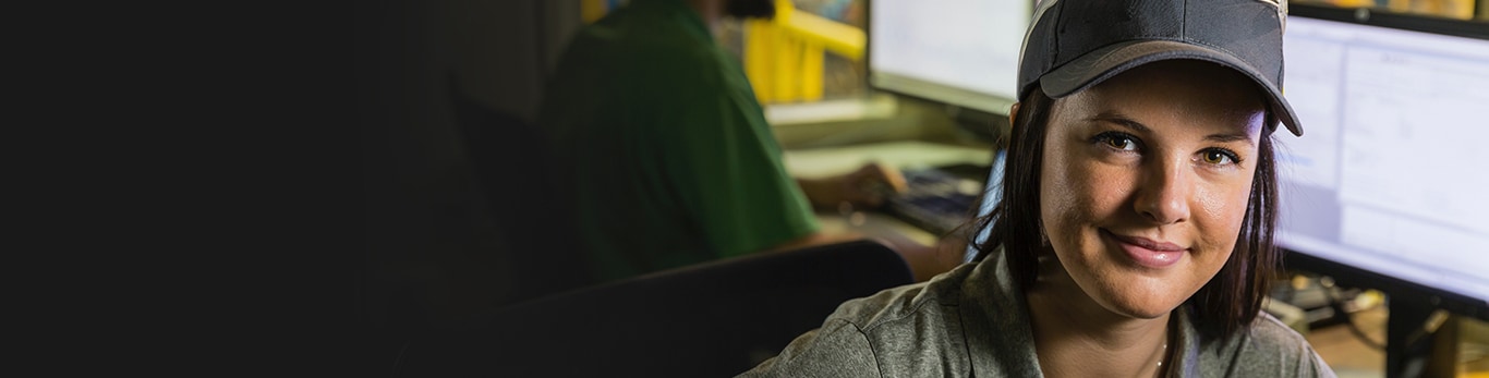 White woman sitting in front of computer monitors looking toward the camera