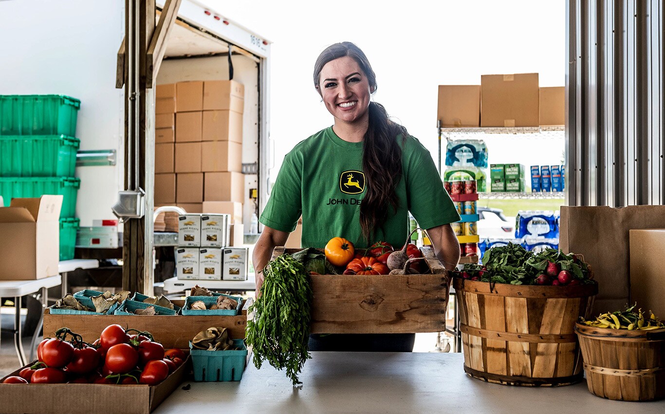 A woman in a John Deere shirt smiles as she serves fresh produce