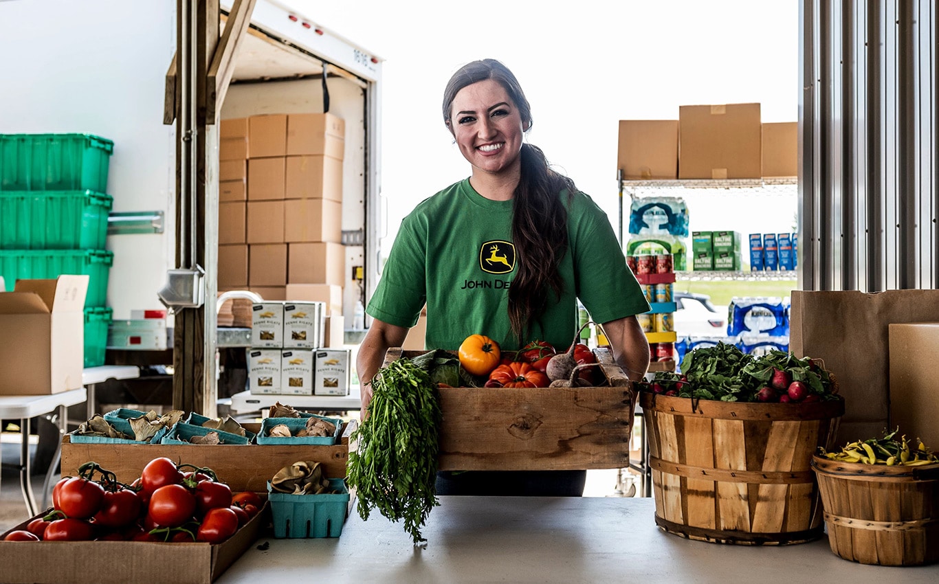 A woman in a John Deere shirt smiles as she serves fresh produce