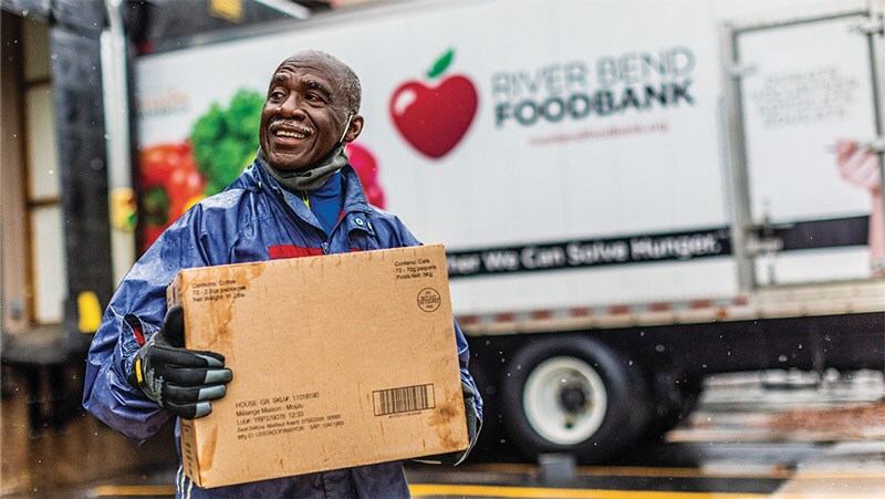 A smiling man carrying a box from a River Bend Food Bank truck