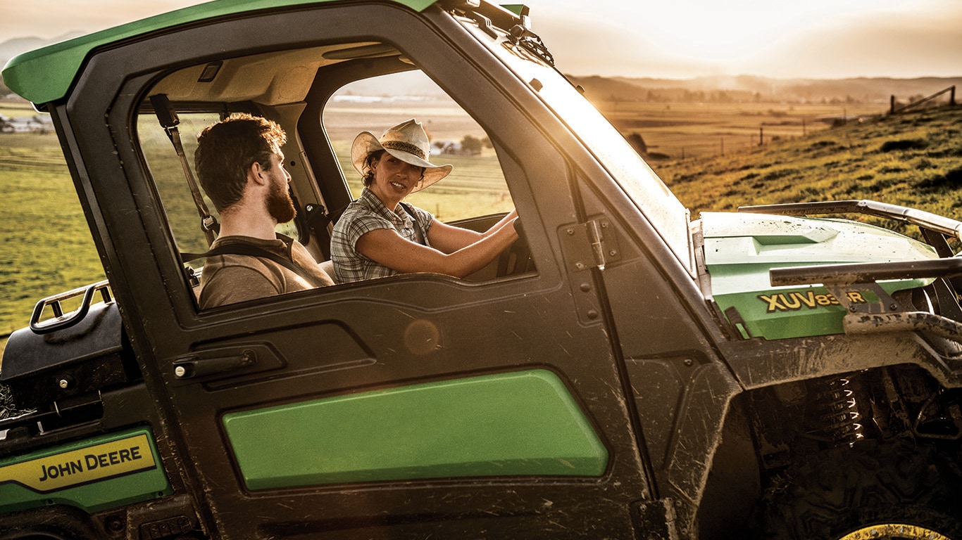 a woman and man riding a gator through a hilly field