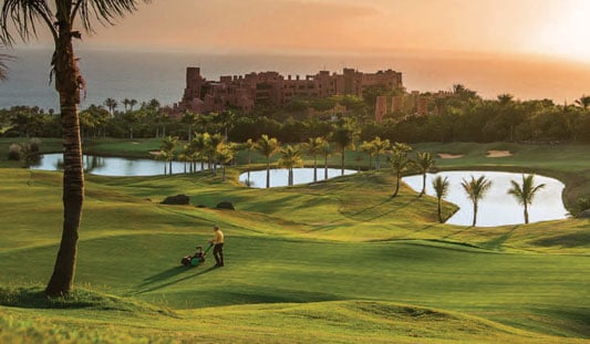 A man mowing along a fairway at dawn