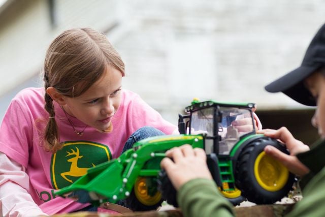 a child wearing a pink John&nbsp;Deere t-shirt playing with a toy John&nbsp;Deere tractor