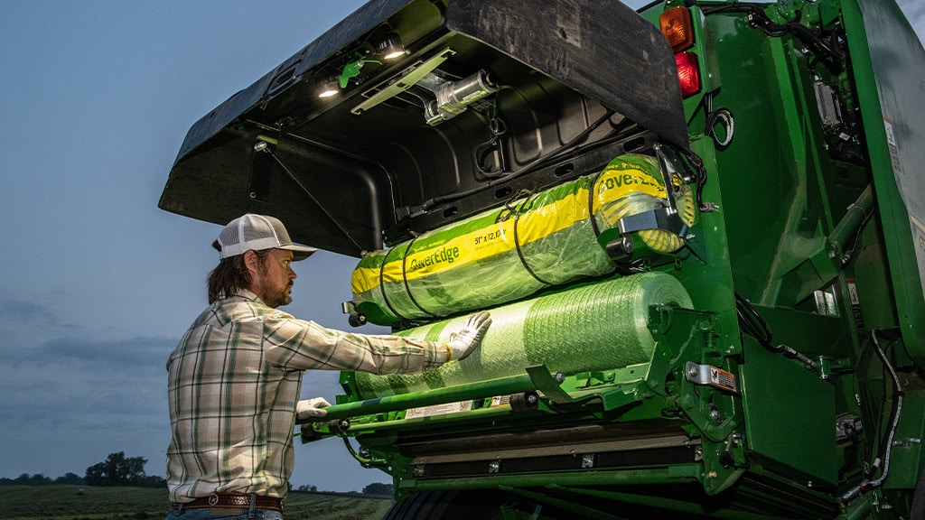 Man loading net wrap into baler at night with net lighting illuminating the area 