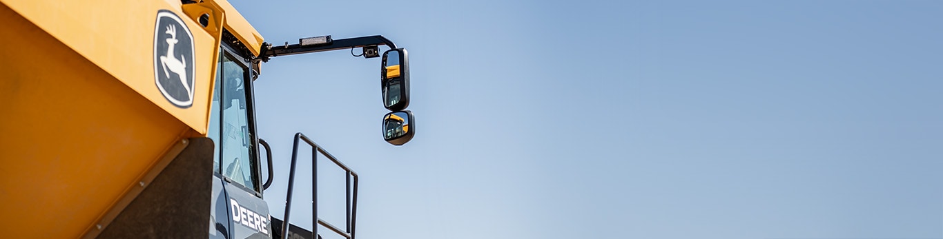Close-up of an articulated dump truck showing logo and side mirrors with blue sky background.
