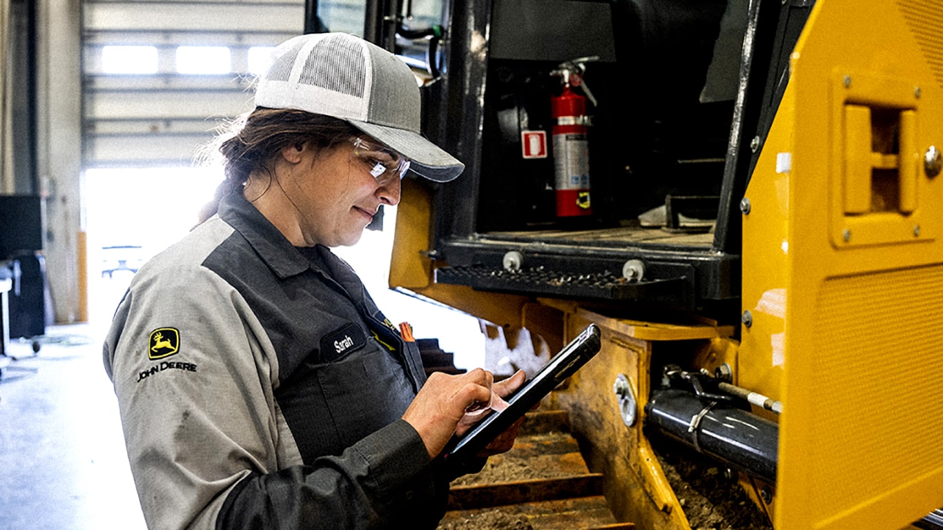 John Deere technician using a tablet in front of a piece of equipment