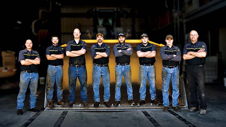 multiple mechanics standing in front of a large yellow plow