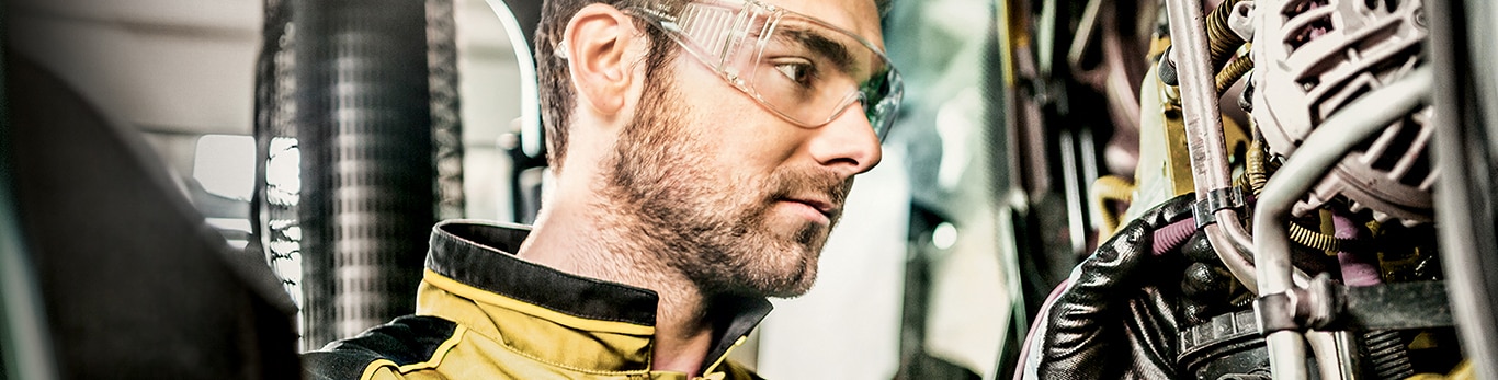 A technician wearing safety goggles looking at a John Deere engine
