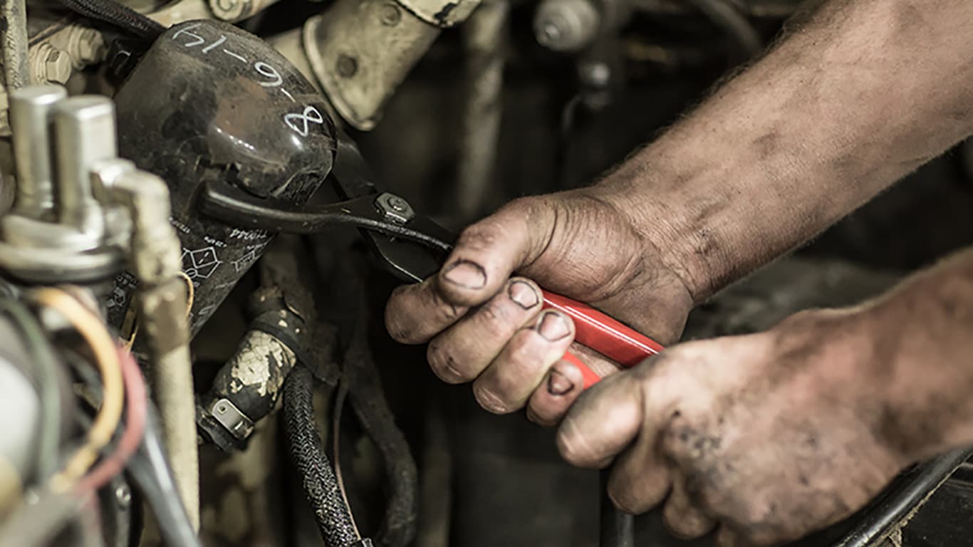 Dirty hands holding wrench adjusting something in John Deere equipment
