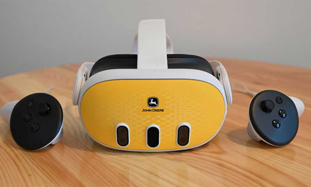 John Deere VR headset with white strap and yellow front panel, with two controllers on a wooden table.