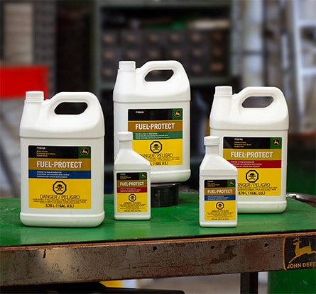 Five containers of John Deere Fuel-Protect additive on a table in a workshop.