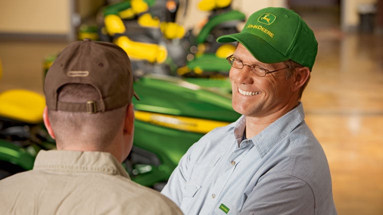  two people in ball caps with tractors in background
