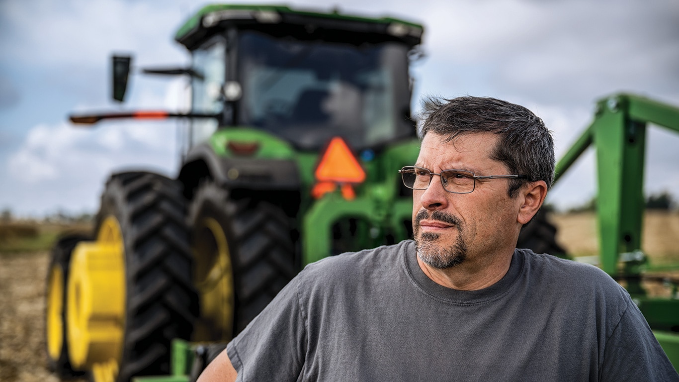 Close-up of a farmer standing in front of a John&nbsp;Deere tractor.