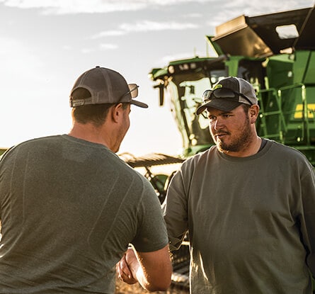 Two people shaking hands in front of a green combine harvester in a field.