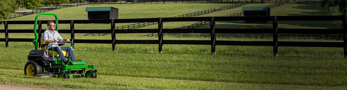 Man driving a z730m mower around a fenced pasture