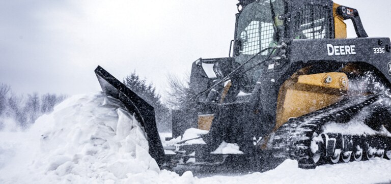 ​A 333G compact track loader with BL9B snow blade attachment plowing snow