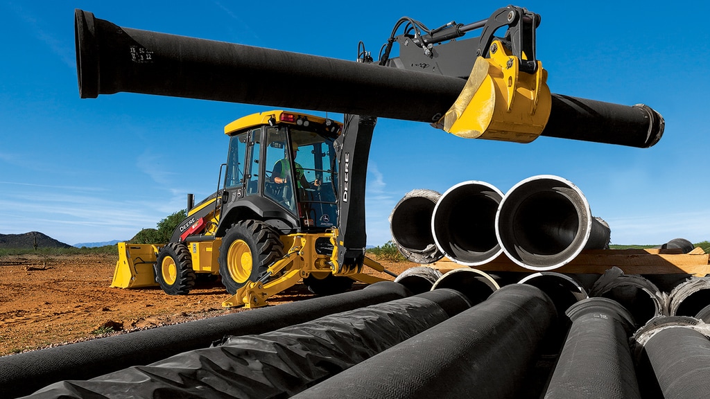  Backhoe 310 G-Tier using a front loader to lift a large heavy industrial metal pipe