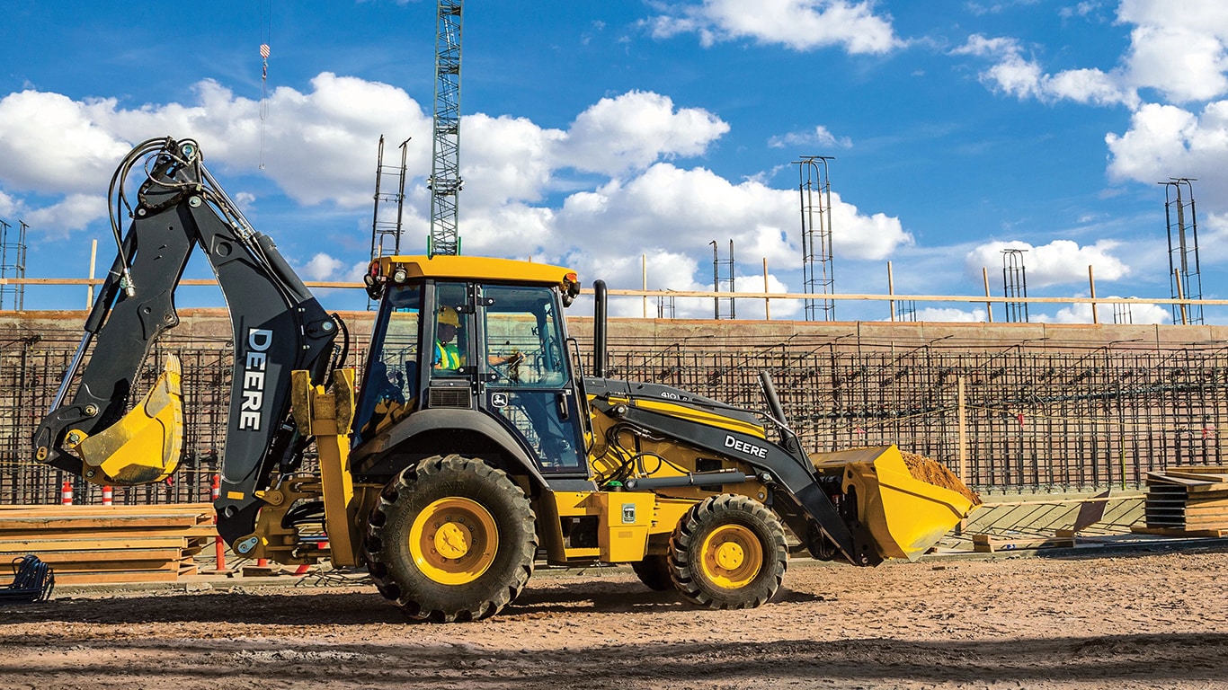 A 410P Backhoe with building materials and cranes in the background.
