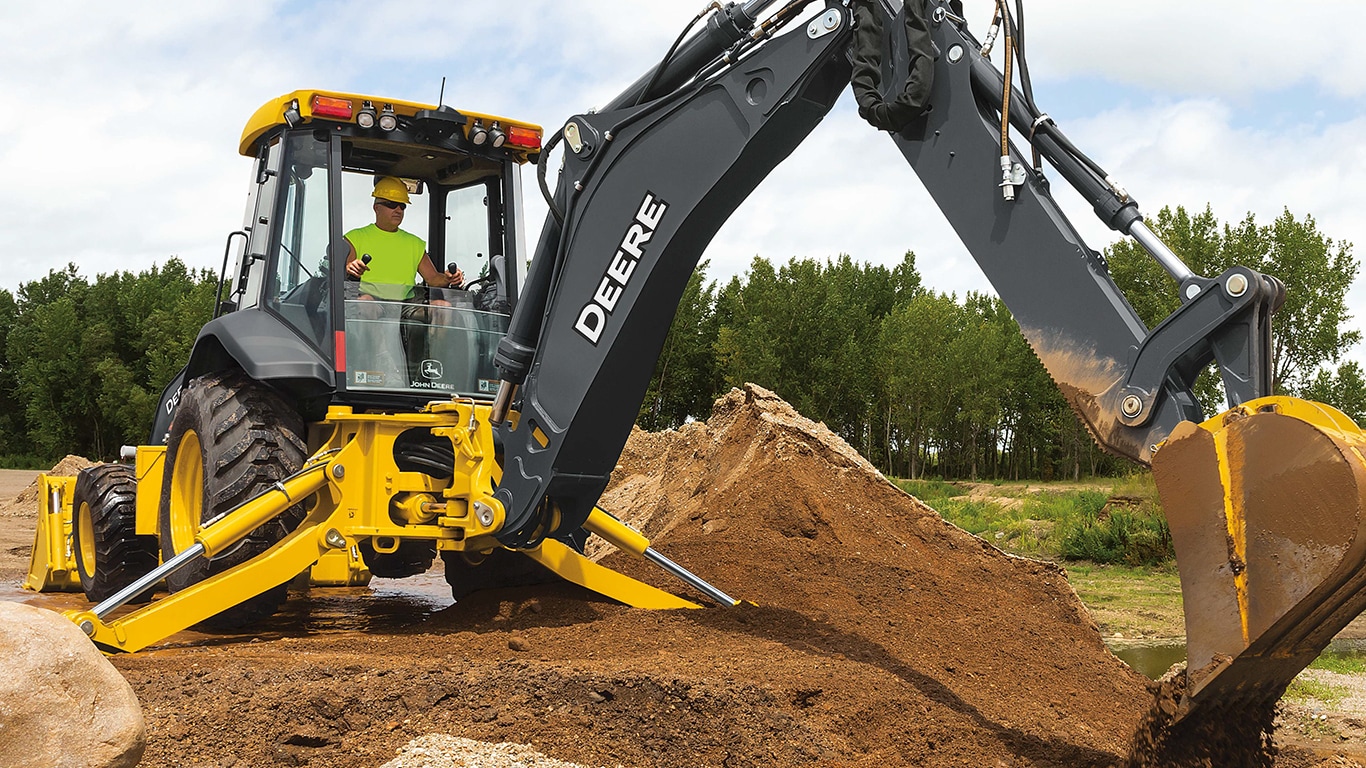 An operator using a 710P-Tier Backhoe to dump dirt in a trench.