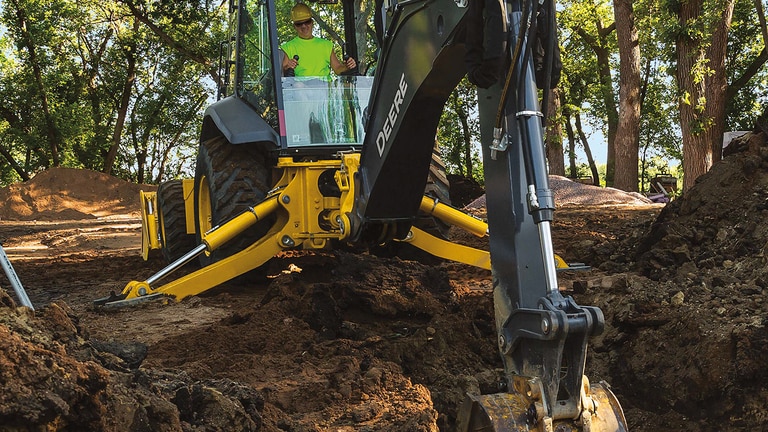 An operator using a 710P-Tier Backhoe to scoop dirt out of a hole.