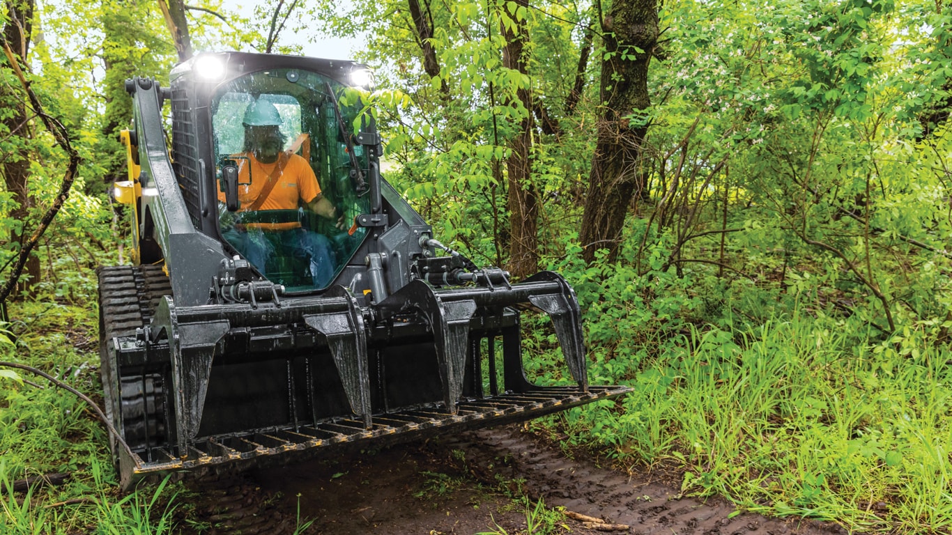 Deere 317G tracked skid steer travels through the woods