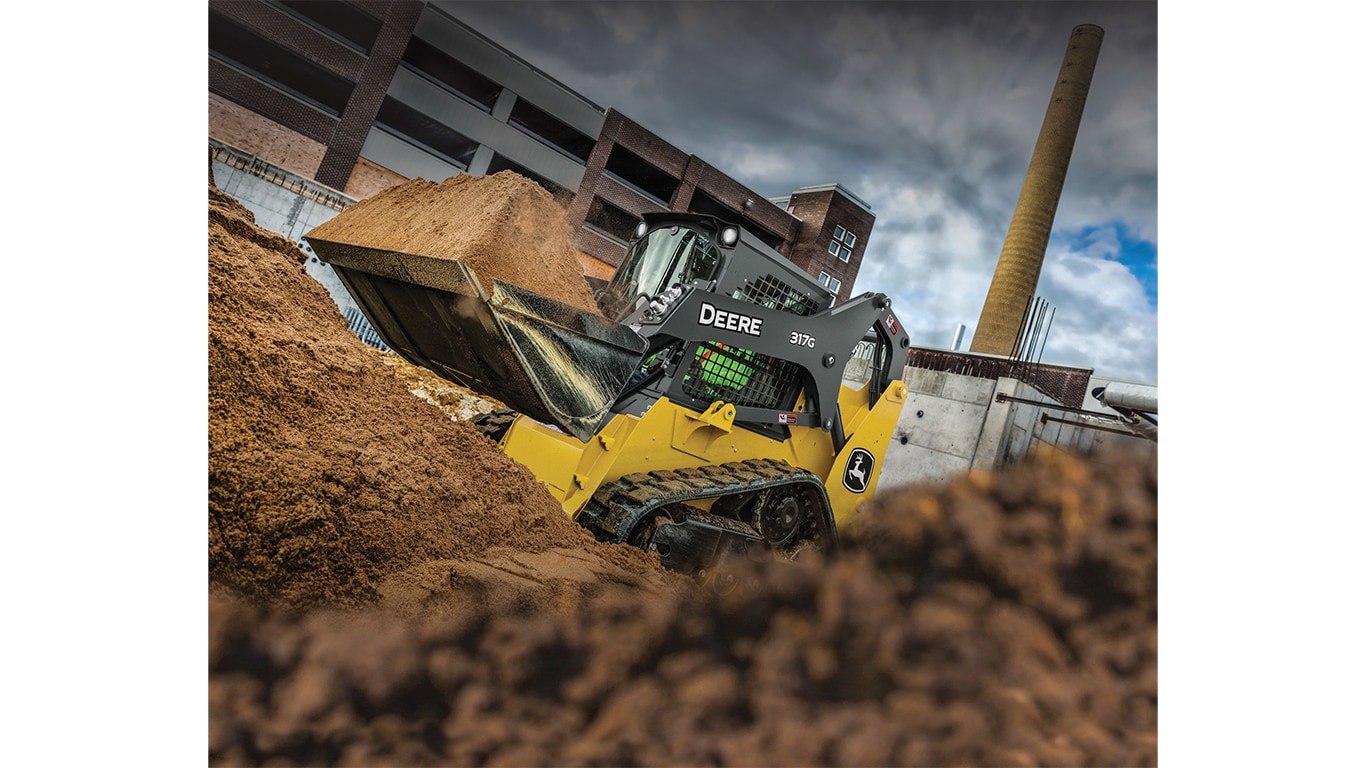 A 317G Compact Track Loader scooping dirt at a worksite.