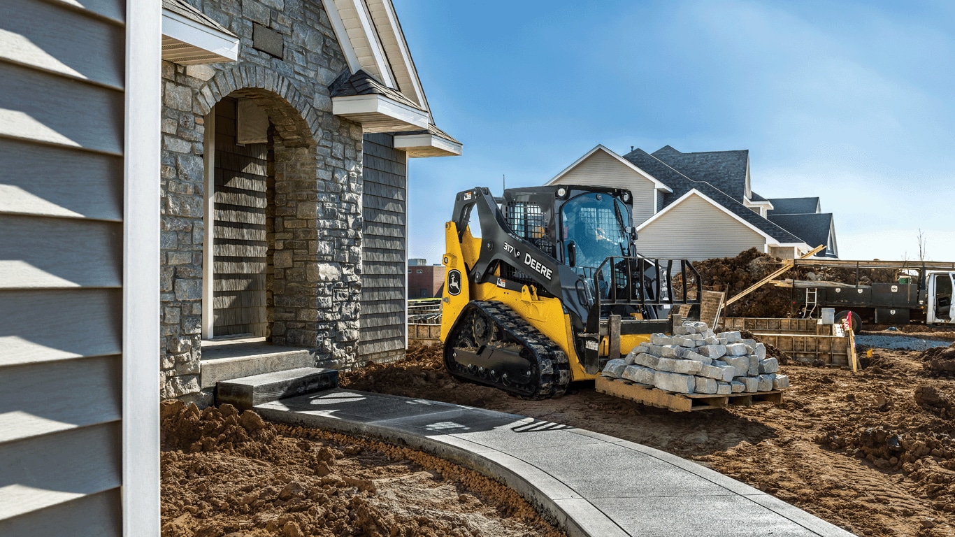 317 P-Tier compact track loader moving pallet of stone for landscaping around house.