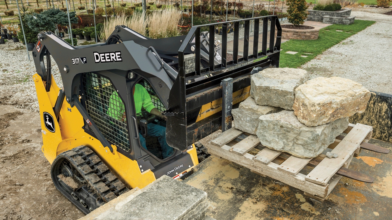 317 P-Tier compact track loader lifting pallet of stone with fork attachment onto truck bed.