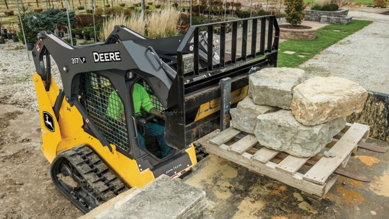 317 P-Tier compact track loader lifting pallet of stone with fork attachment onto truck bed.