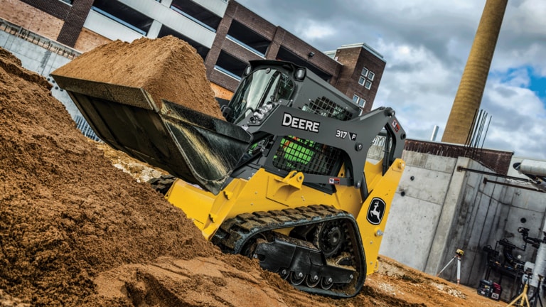 317 P-Tier compact track loader using bucket attachment to move sand on job site.