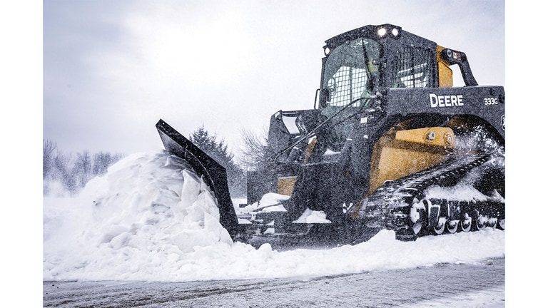 A 333G Compact Track Loader with snow blade attachment plowing snow.