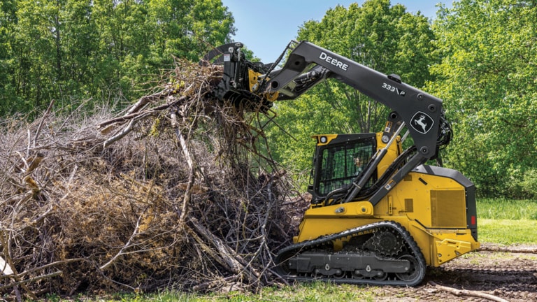 333 P-Tier compact track loader with grapple attachment piling up brush into a pile.