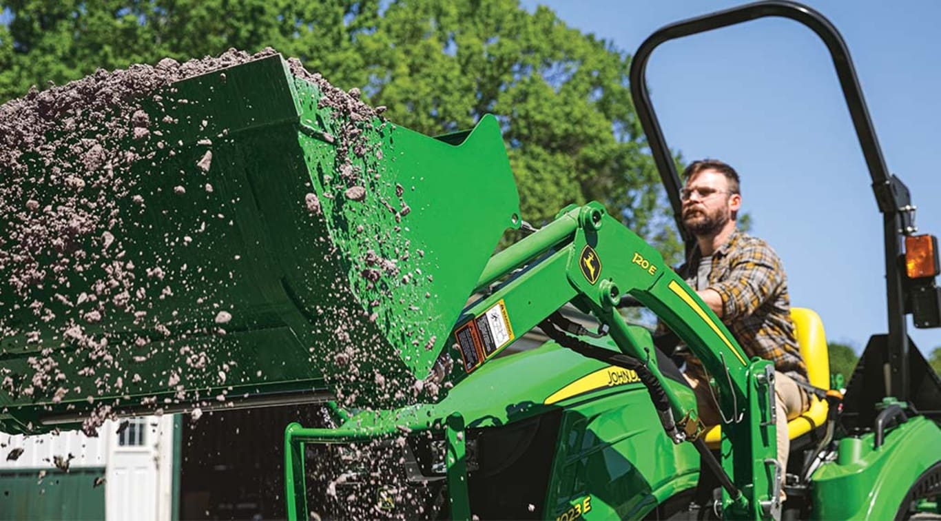 A person using their 1023E Tractor to shovel sediment off the ground.