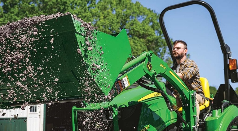 A person using their 1023E Tractor to shovel sediment off the ground.