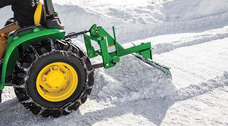 a 3032E Tractor using a snowplow attachment and snow chains attached to the tires.