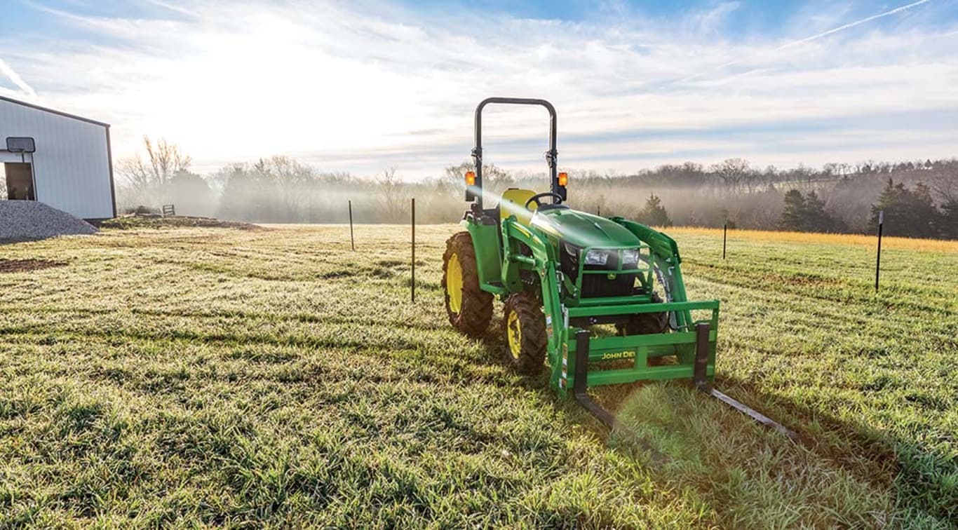 The sun shining behind a 3038E Tractor posed in a field.