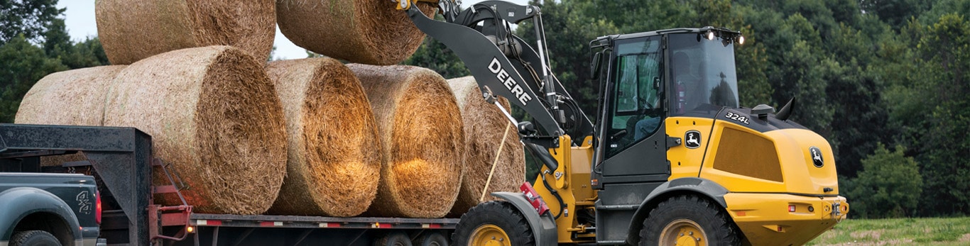 324L Compact Loader lifts a round bale onto a trailer with a bale spear attachment