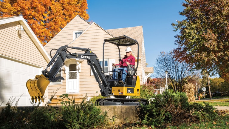 Man using a 17G excavator to move landscaping in front of a house.