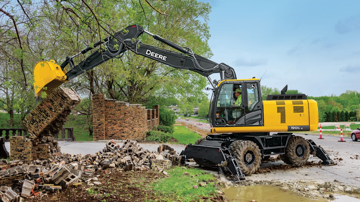 A 190GW Excavator being used to break down a brick wall in front of a road.