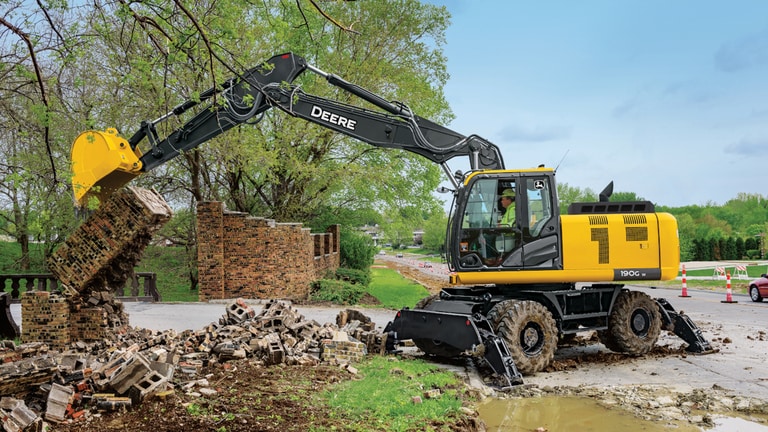 A 190GW Excavator being used to break down a brick wall in front of a road.